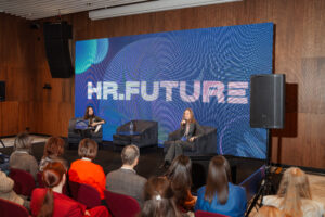 В центре внимания — ярко освещенная сцена, где выступают два спикера.